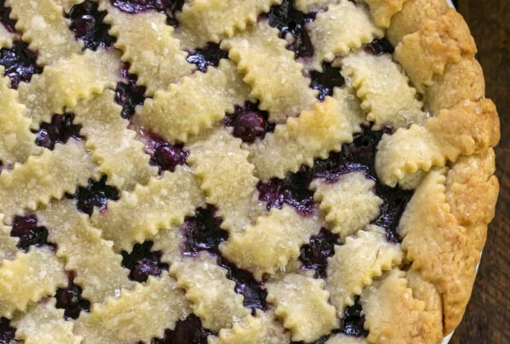 Golden lattice-top blueberry pie cooling on a wire rack, deep purple filling bubbling through the woven crust, dusted with coarse sugar, summer sunlight overhead