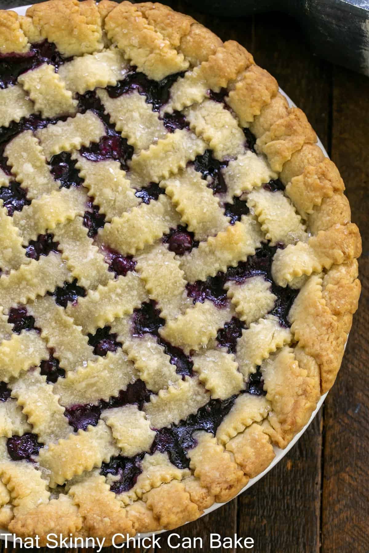 Golden lattice-top blueberry pie cooling on a wire rack, deep purple filling bubbling through the woven crust, dusted with coarse sugar, summer sunlight overhead