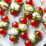 Caprese skewers with cherry tomatoes, fresh mozzarella, and basil on a white marble board drizzled with balsamic glaze