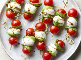 Caprese skewers with cherry tomatoes, fresh mozzarella, and basil on a white marble board drizzled with balsamic glaze