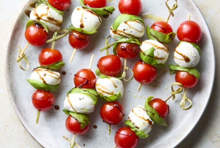 Caprese skewers with cherry tomatoes, fresh mozzarella, and basil on a white marble board drizzled with balsamic glaze