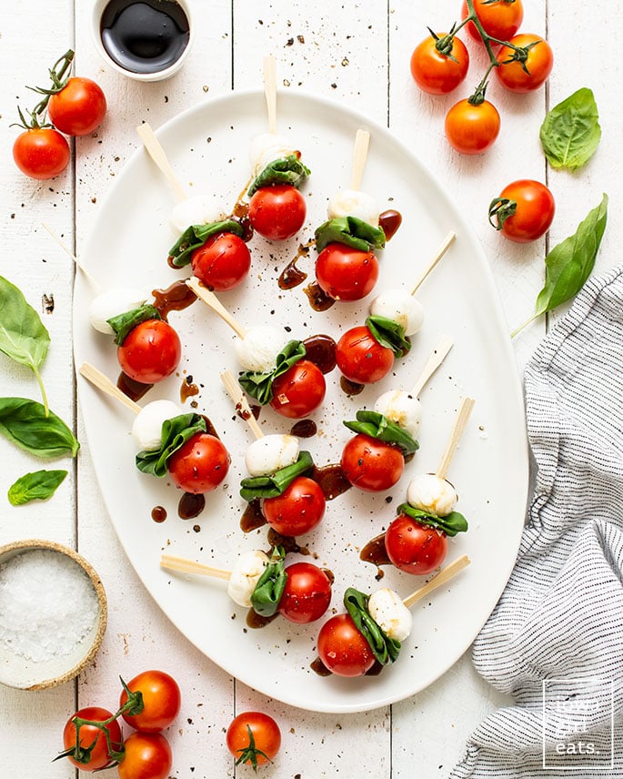 Close-up of Caprese skewers on a slate board with balsamic glaze drizzle and fresh basil garnish, served at a summer party