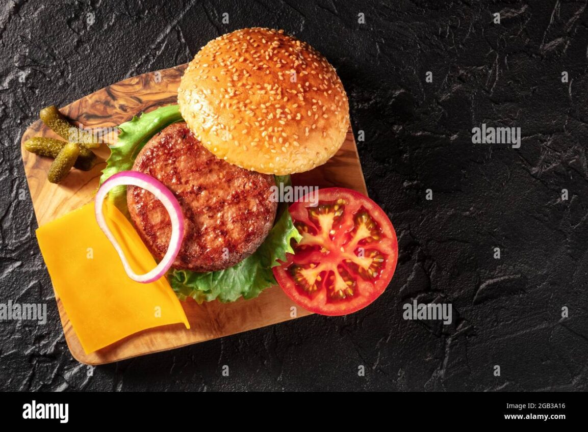 Overhead flat lay of classic cheeseburger ingredients including ground beef patties, American cheese slices, brioche buns, tomato, onion, lettuce, pickles, and condiments on a rustic wooden surface