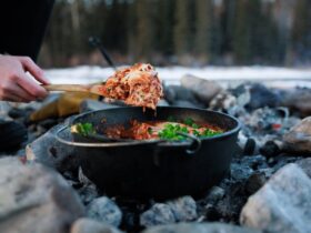 Dutch oven lasagna with bubbling cheese and golden top served at a campsite with pine trees in the background