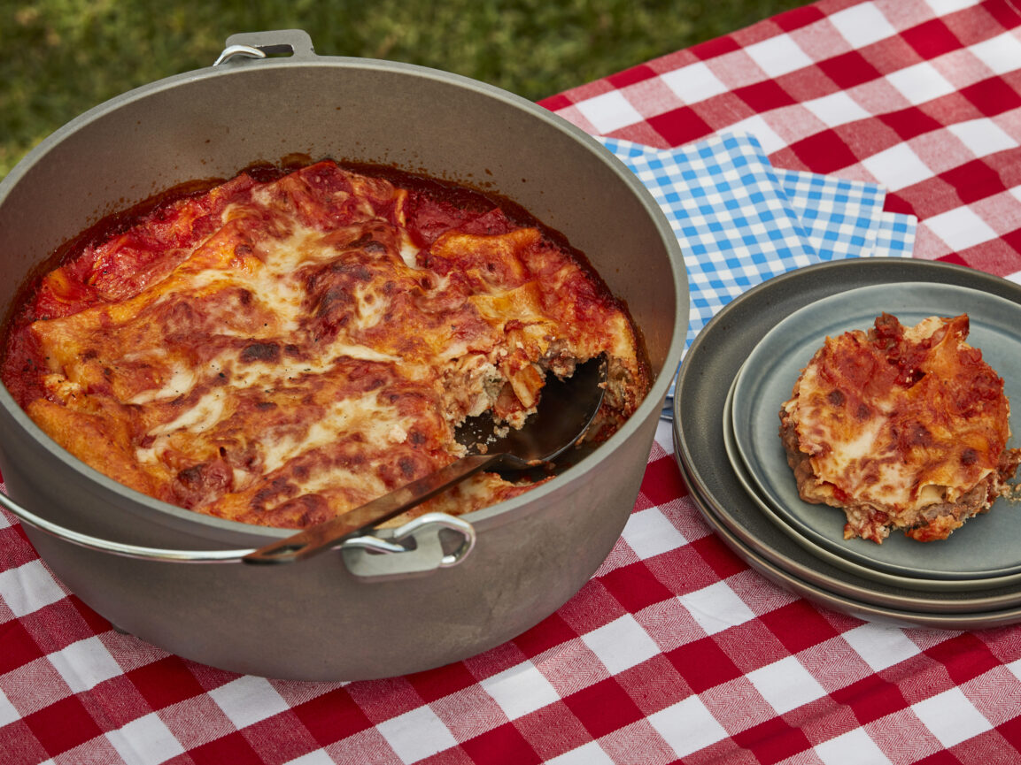 Ingredients for Dutch oven lasagna laid out at a campsite including sausage, ricotta, mozzarella, marinara sauce and dry no-boil noodles
