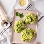 Garlic Parmesan Zoodles served in a white bowl with golden garlic butter sauce, shaved Parmesan, fresh basil, and cracked black pepper