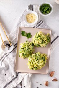 Garlic Parmesan Zoodles served in a white bowl with golden garlic butter sauce, shaved Parmesan, fresh basil, and cracked black pepper