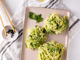Garlic Parmesan Zoodles served in a white bowl with golden garlic butter sauce, shaved Parmesan, fresh basil, and cracked black pepper