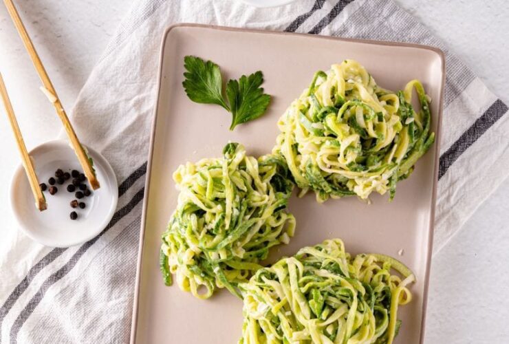 Garlic Parmesan Zoodles served in a white bowl with golden garlic butter sauce, shaved Parmesan, fresh basil, and cracked black pepper