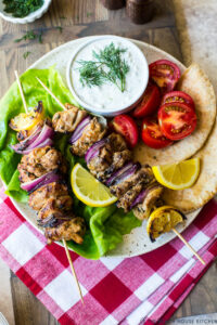 Grilled chicken skewers with tzatziki sauce served on a wooden platter with warm pita, sliced cucumber, and fresh dill garnish
