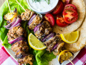 Grilled chicken skewers with tzatziki sauce served on a wooden platter with warm pita, sliced cucumber, and fresh dill garnish