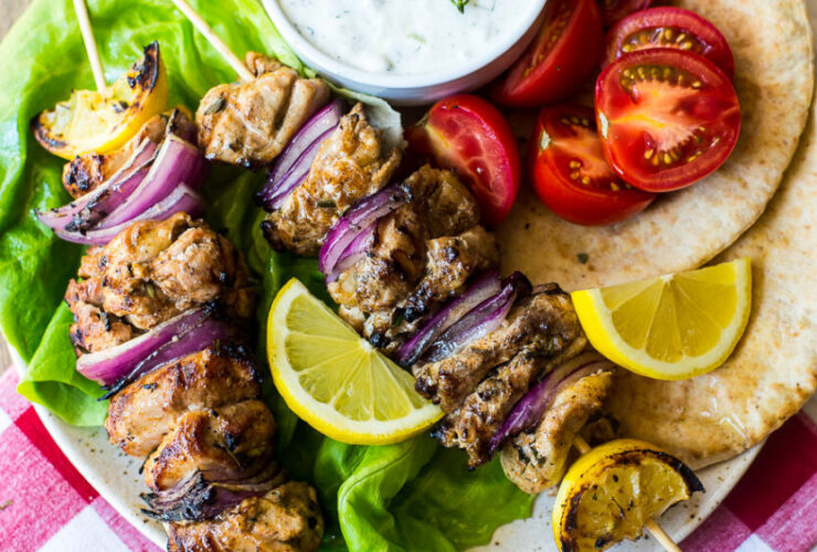 Grilled chicken skewers with tzatziki sauce served on a wooden platter with warm pita, sliced cucumber, and fresh dill garnish