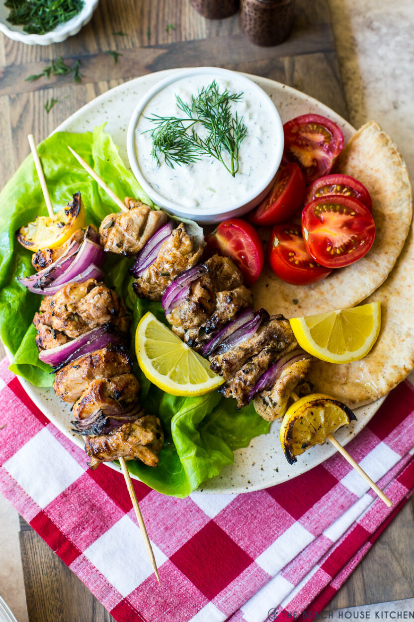 Grilled chicken skewers with tzatziki sauce served on a wooden platter with warm pita, sliced cucumber, and fresh dill garnish
