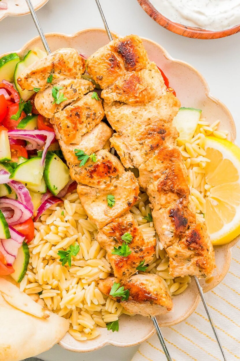Flat lay of marinated chicken thighs in a zip-lock bag alongside bowls of Greek yogurt, grated cucumber, garlic, lemon, and fresh dill for tzatziki preparation