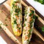 Grilled corn on the cob elote style with charred kernels, melted butter, Parmesan, chili powder, and lime on a rustic wooden board
