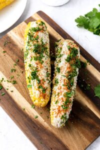 Grilled corn on the cob elote style with charred kernels, melted butter, Parmesan, chili powder, and lime on a rustic wooden board