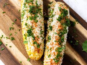 Grilled corn on the cob elote style with charred kernels, melted butter, Parmesan, chili powder, and lime on a rustic wooden board
