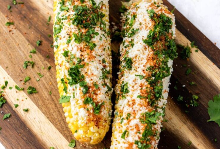 Grilled corn on the cob elote style with charred kernels, melted butter, Parmesan, chili powder, and lime on a rustic wooden board