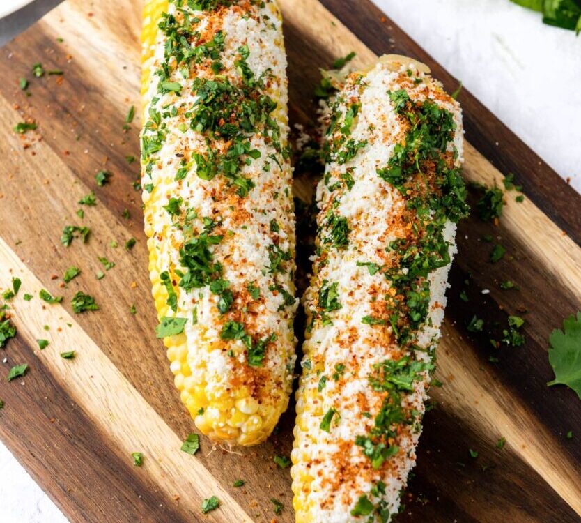 Grilled corn on the cob elote style with charred kernels, melted butter, Parmesan, chili powder, and lime on a rustic wooden board
