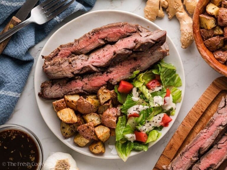 Flank steak in a zip-lock bag submerged in dark marinade with lime slices and garlic cloves visible — flat lay ingredients and process shot