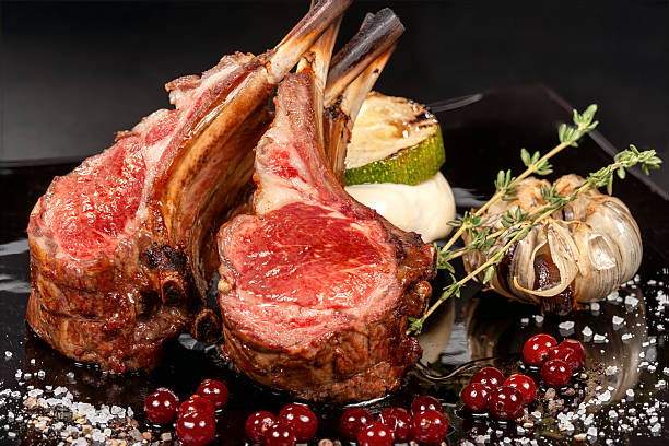 Close-up of a grilled lamb chop sliced to reveal a blush-pink medium-rare center, resting on a bed of fresh herbs with a lemon wedge and sea salt flakes on a dark slate board