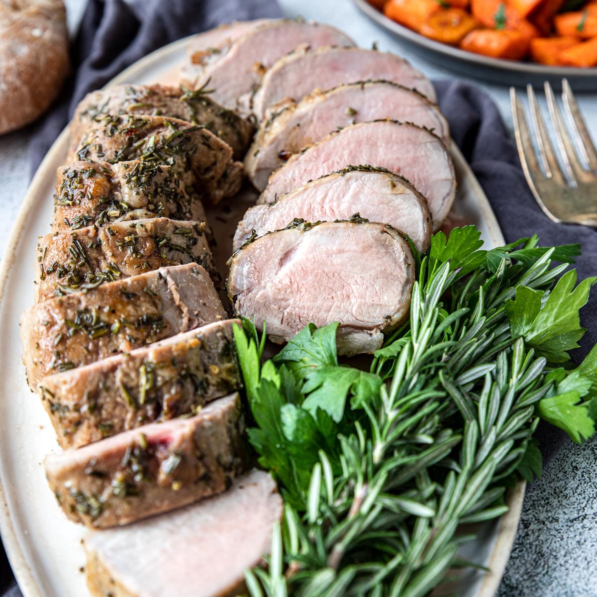 Pork tenderloin in a zip-lock bag with marinade, garlic cloves, fresh rosemary sprigs, smoked paprika, and olive oil on a marble surface