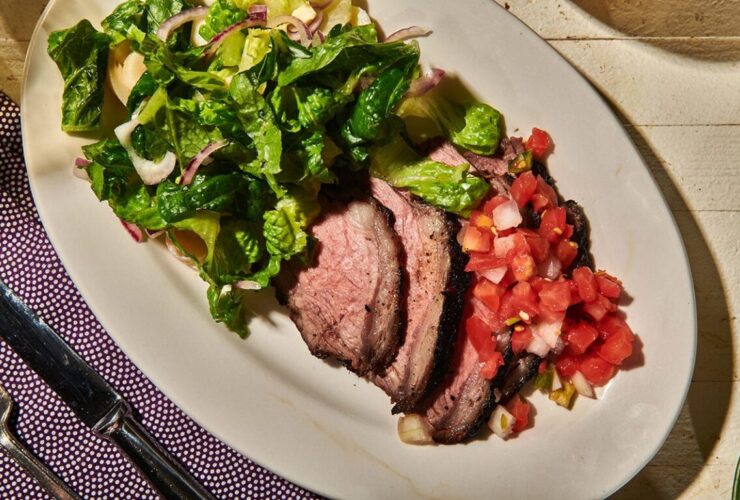 Grilled tri-tip sliced against the grain on a wooden cutting board, showing a smoky charred crust and pink juicy interior, garnished with fresh herbs