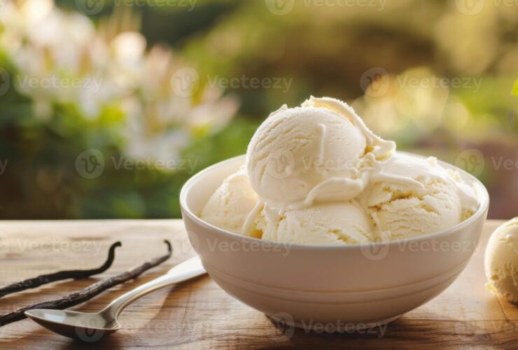 Homemade vanilla ice cream scooped into a white ceramic bowl, golden and creamy with visible vanilla bean specks, styled on a rustic wooden table with a linen napkin and fresh vanilla pods