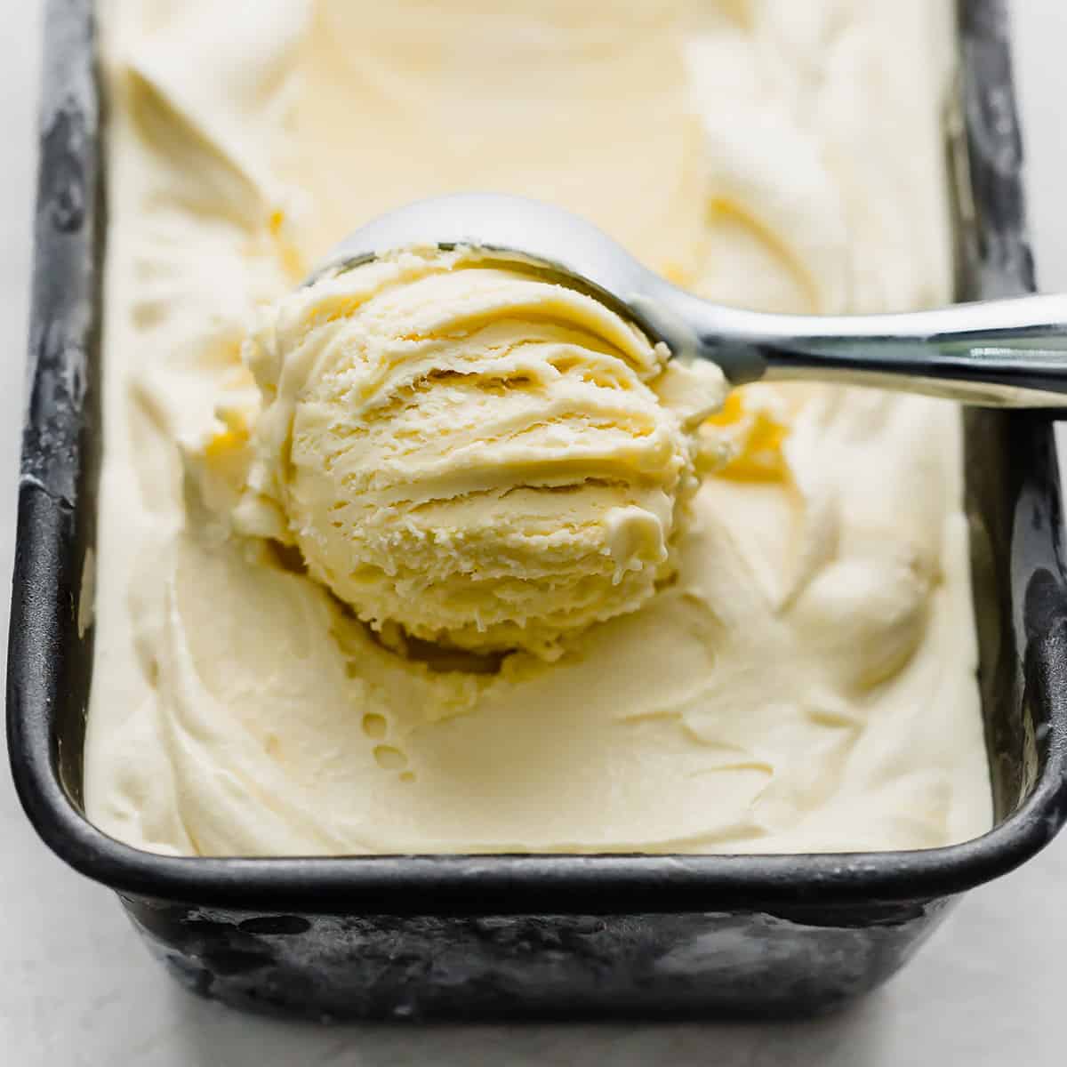 Overhead flat lay of vanilla ice cream ingredients — heavy cream, egg yolks, vanilla bean pods, whole milk, and sugar — arranged on a white marble surface with a copper saucepan