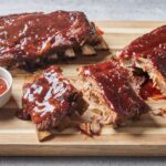Instant Pot ribs glazed with sticky barbecue sauce, fall-off-the-bone tender, served on a wooden board with fresh herbs and sauce on the side