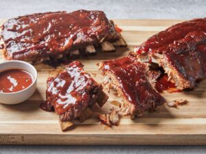 Instant Pot ribs glazed with sticky barbecue sauce, fall-off-the-bone tender, served on a wooden board with fresh herbs and sauce on the side