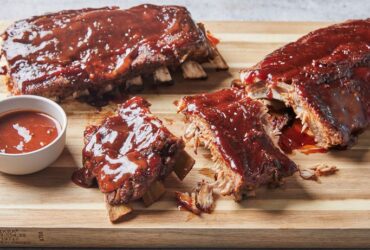 Instant Pot ribs glazed with sticky barbecue sauce, fall-off-the-bone tender, served on a wooden board with fresh herbs and sauce on the side