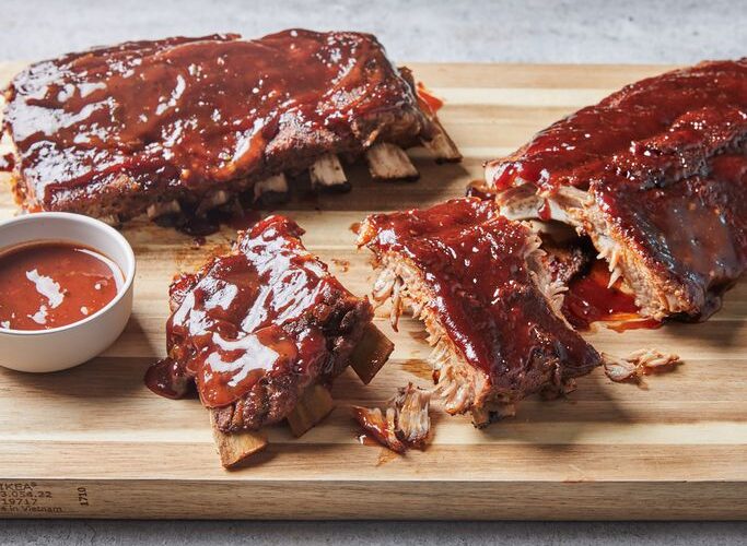 Instant Pot ribs glazed with sticky barbecue sauce, fall-off-the-bone tender, served on a wooden board with fresh herbs and sauce on the side