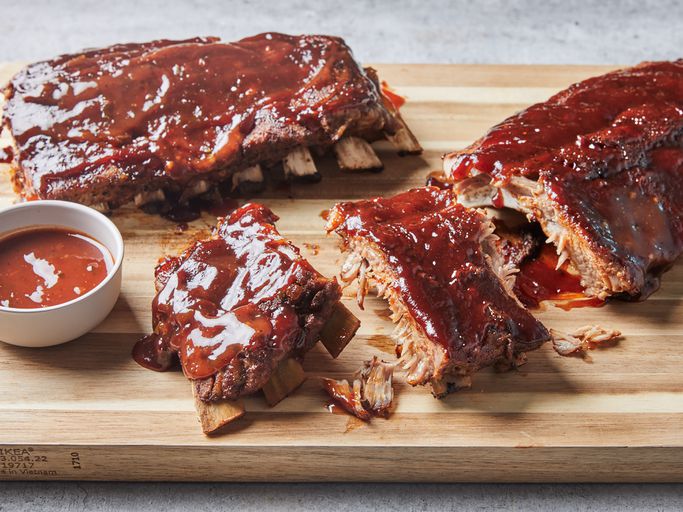Instant Pot ribs glazed with sticky barbecue sauce, fall-off-the-bone tender, served on a wooden board with fresh herbs and sauce on the side