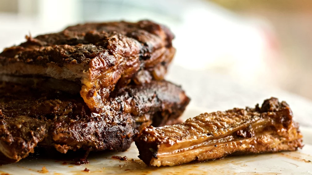 Baby back ribs coated in dry rub spice mixture laid out on a cutting board next to Instant Pot, apple cider vinegar, and barbecue sauce ingredients
