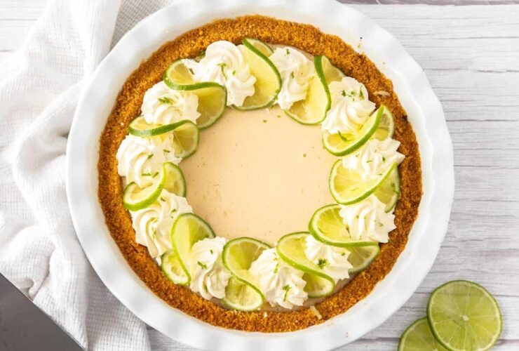 Key Lime Pie with whipped cream and lime slices on a white plate, overhead shot