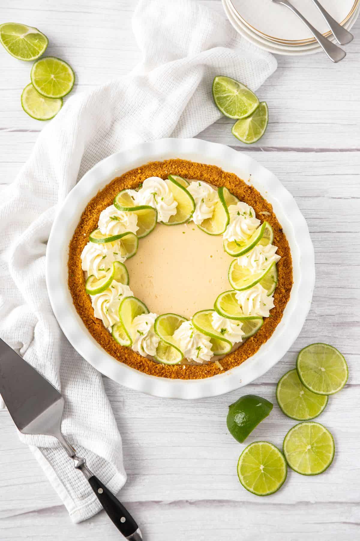 Key Lime Pie with whipped cream and lime slices on a white plate, overhead shot
