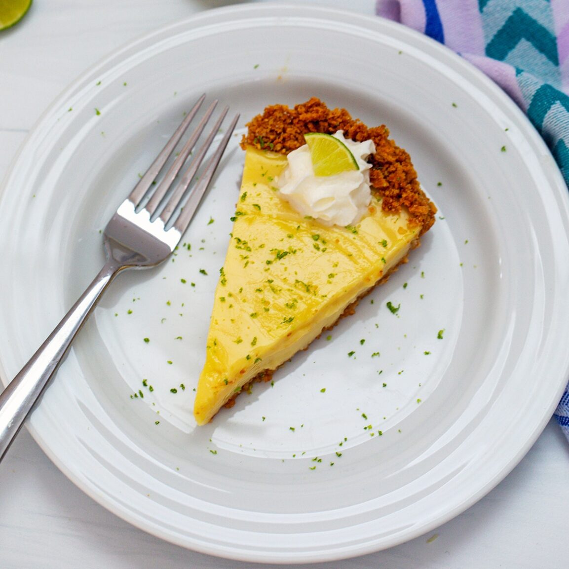 Close-up slice of Key Lime Pie with whipped cream, lime zest, and a golden graham cracker crust on a fork