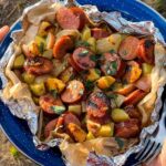 Kielbasa and potato foil packets opened on a plate showing smoky sausage slices, golden roasted potatoes, and melted butter glaze with a spicy mustard drizzle