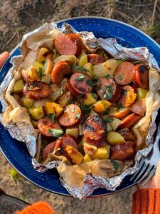 Kielbasa and potato foil packets opened on a plate showing smoky sausage slices, golden roasted potatoes, and melted butter glaze with a spicy mustard drizzle