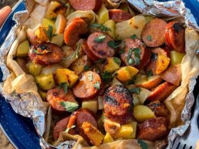 Kielbasa and potato foil packets opened on a plate showing smoky sausage slices, golden roasted potatoes, and melted butter glaze with a spicy mustard drizzle