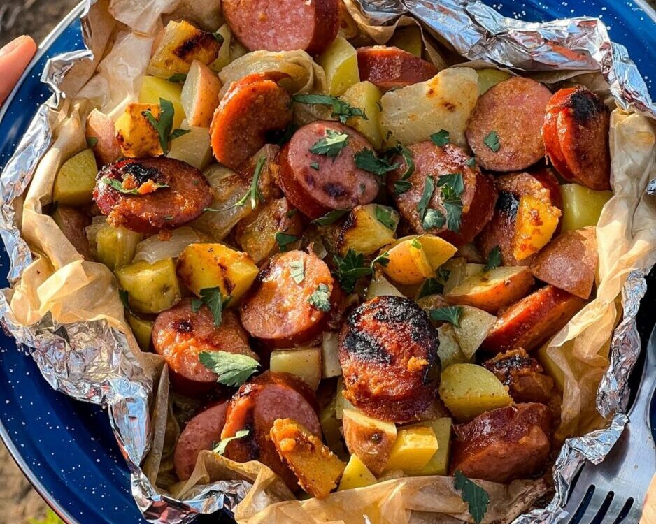 Kielbasa and potato foil packets opened on a plate showing smoky sausage slices, golden roasted potatoes, and melted butter glaze with a spicy mustard drizzle