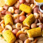 Low Country Shrimp Boil with shrimp, andouille sausage, corn on the cob, and red potatoes dumped on a newspaper-lined table with melted butter and lemon wedges