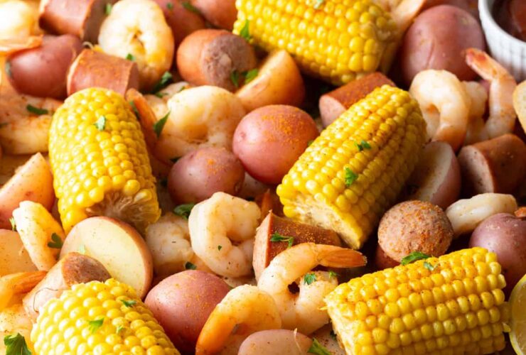 Low Country Shrimp Boil with shrimp, andouille sausage, corn on the cob, and red potatoes dumped on a newspaper-lined table with melted butter and lemon wedges