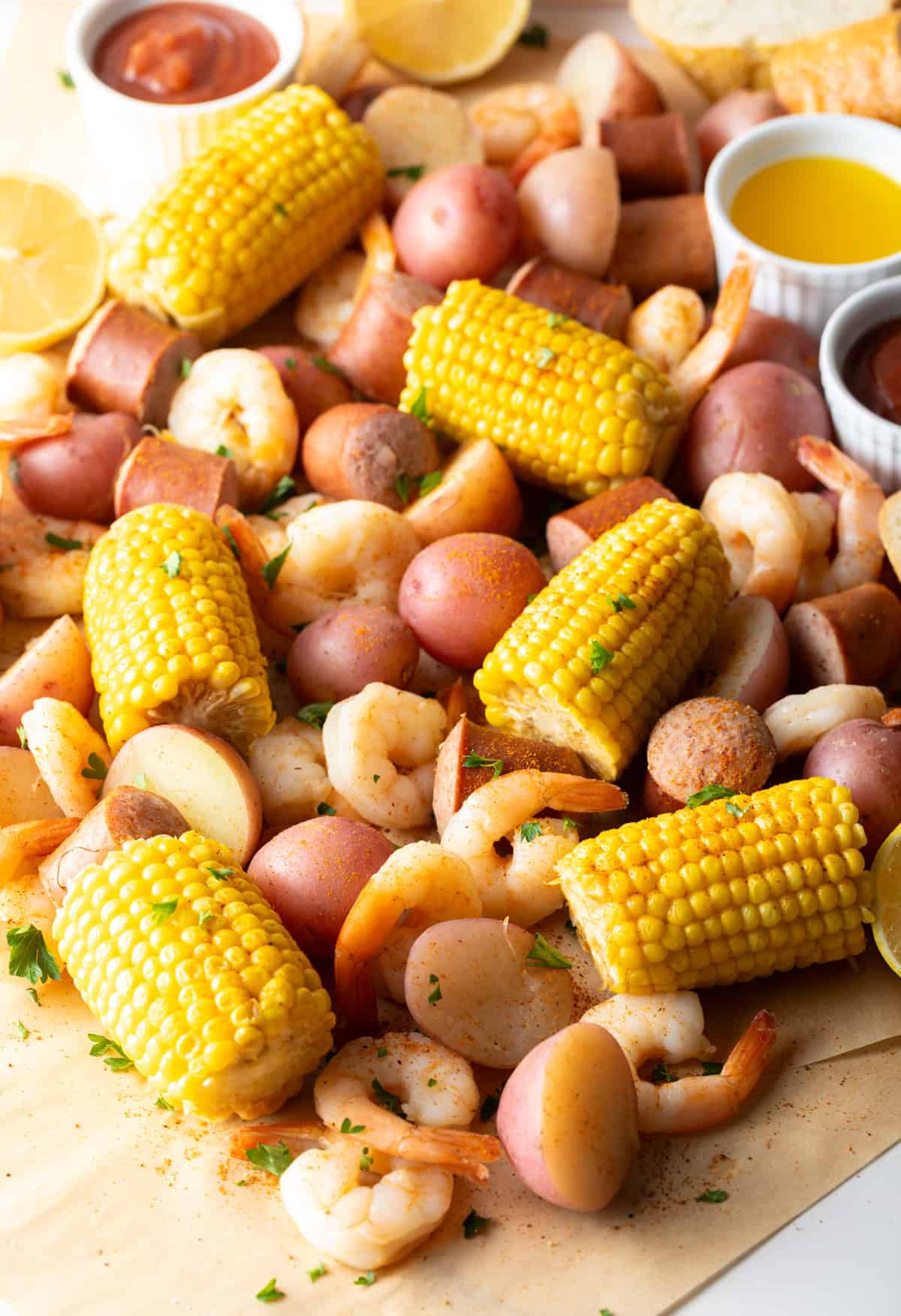Low Country Shrimp Boil with shrimp, andouille sausage, corn on the cob, and red potatoes dumped on a newspaper-lined table with melted butter and lemon wedges