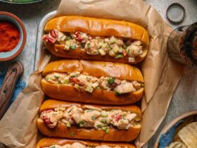 Classic Maine Lobster Roll served in a golden toasted split-top bun overflowing with creamy lobster salad, garnished with fresh chives, served on parchment with lemon wedges and kettle chips on a rustic wooden board outdoors