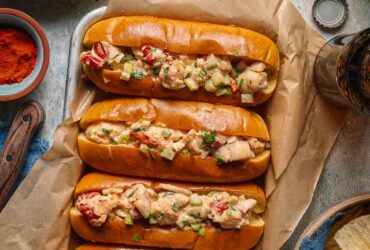 Classic Maine Lobster Roll served in a golden toasted split-top bun overflowing with creamy lobster salad, garnished with fresh chives, served on parchment with lemon wedges and kettle chips on a rustic wooden board outdoors