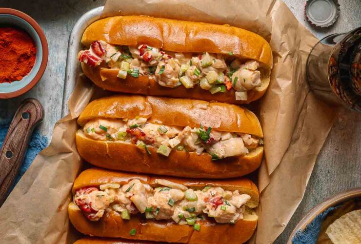 Classic Maine Lobster Roll served in a golden toasted split-top bun overflowing with creamy lobster salad, garnished with fresh chives, served on parchment with lemon wedges and kettle chips on a rustic wooden board outdoors