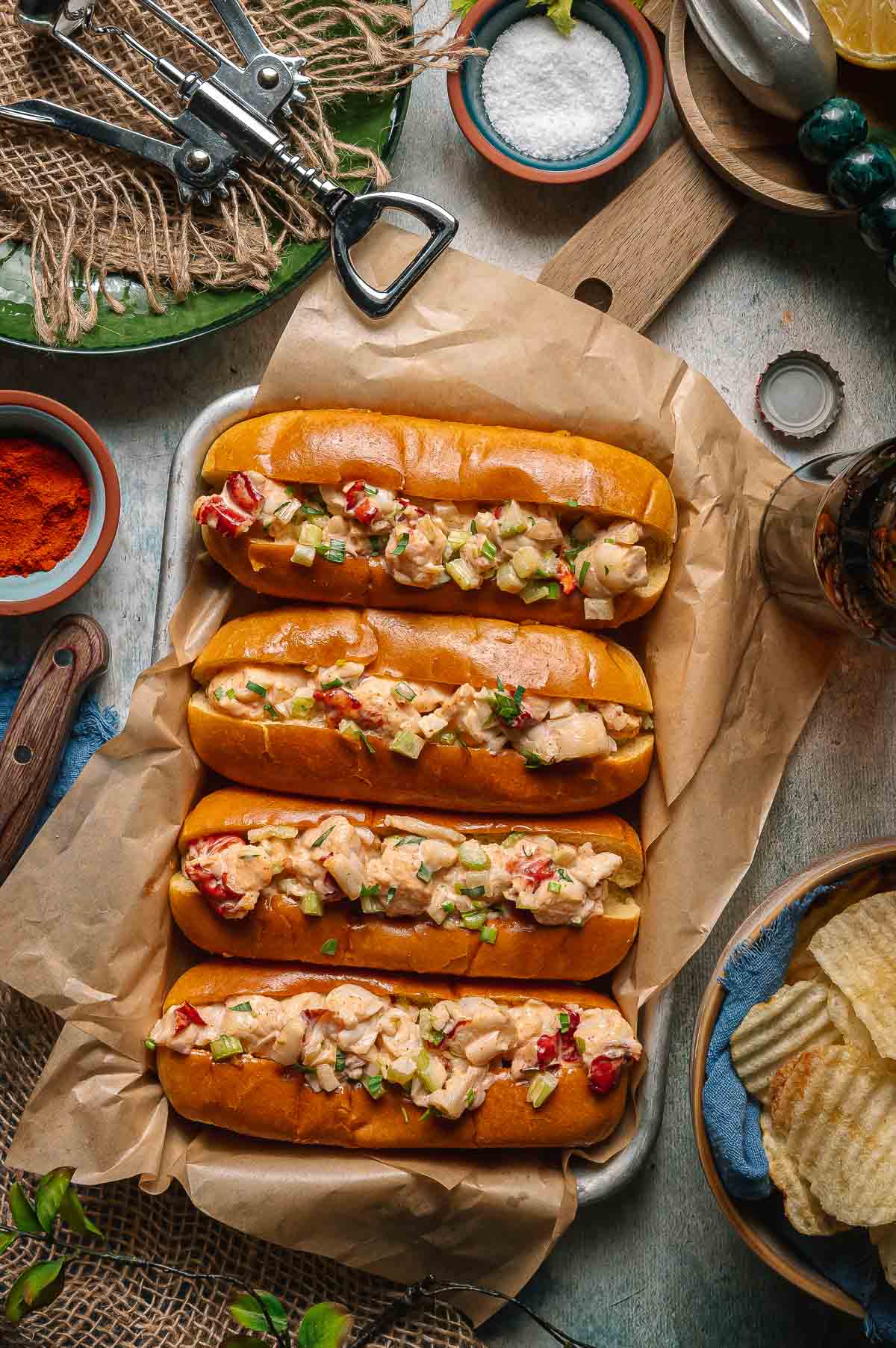 Classic Maine Lobster Roll served in a golden toasted split-top bun overflowing with creamy lobster salad, garnished with fresh chives, served on parchment with lemon wedges and kettle chips on a rustic wooden board outdoors