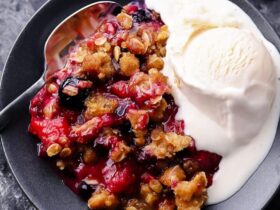 Mixed Berry Crisp with golden oat crumble topping served warm in a white baking dish with a scoop of melting vanilla ice cream, overhead shot on a rustic wooden table